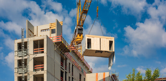Crane lifting a prefabricated wooden building module to its position in the structure.